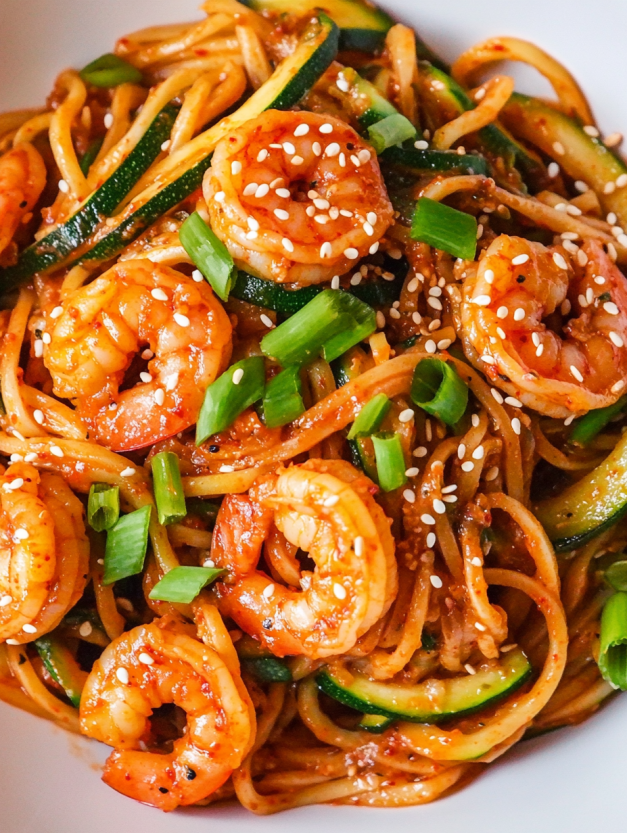 A bowl of noodles with shrimp and zucchini.